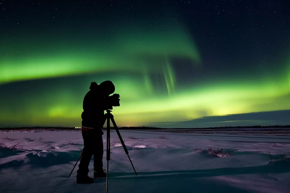 Man taking a pictures of Northern Lights at night with a camera